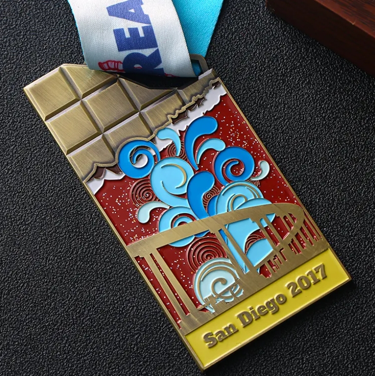 Unique medal shaped like a chocolate bar, with colorful enamel design showing San Diego - themed elements (bridge, waves). Inscribed “San Diego 2017” and paired with a “REAT C” ribbon. Ideal for comme