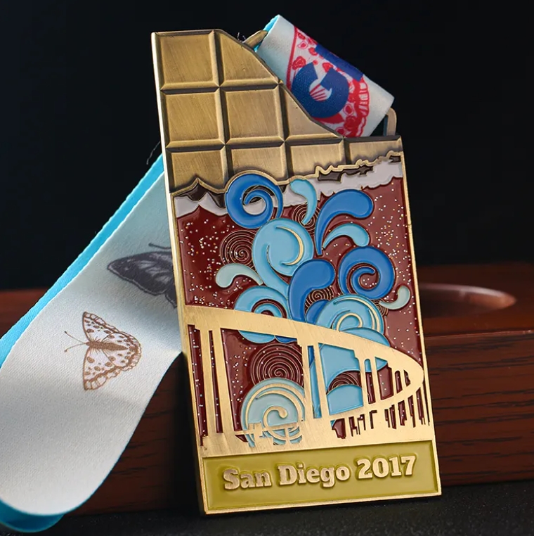 Unique medal shaped like a chocolate bar, with colorful enamel design showing San Diego - themed elements (bridge, waves). Inscribed “San Diego 2017” and paired with a “REAT C” ribbon. Ideal for comme
