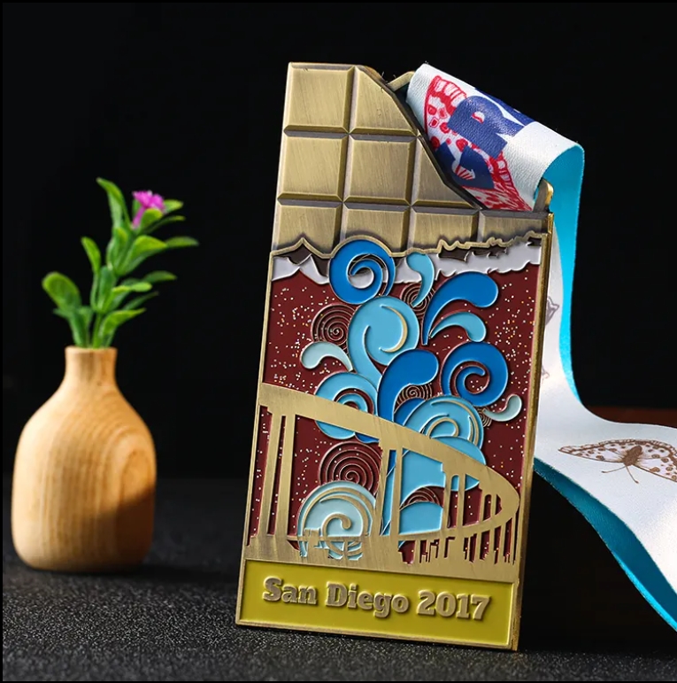Unique medal shaped like a chocolate bar, with colorful enamel design showing San Diego - themed elements (bridge, waves). Inscribed “San Diego 2017” and paired with a “REAT C” ribbon. Ideal for comme